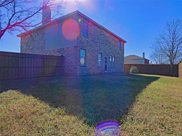 view of home's exterior with a yard, brick siding, a fenced backyard, and a chimney