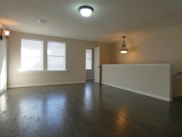 empty room with dark wood-style floors, visible vents, a textured ceiling, and baseboards