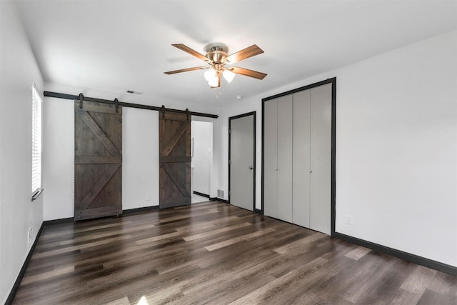 unfurnished bedroom with a barn door, wood finished floors, baseboards, and ceiling fan
