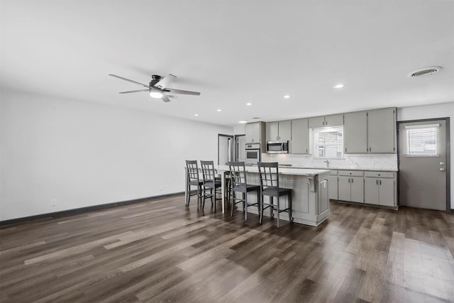 kitchen featuring stainless steel appliances, gray cabinets, a kitchen bar, dark wood finished floors, and a kitchen island