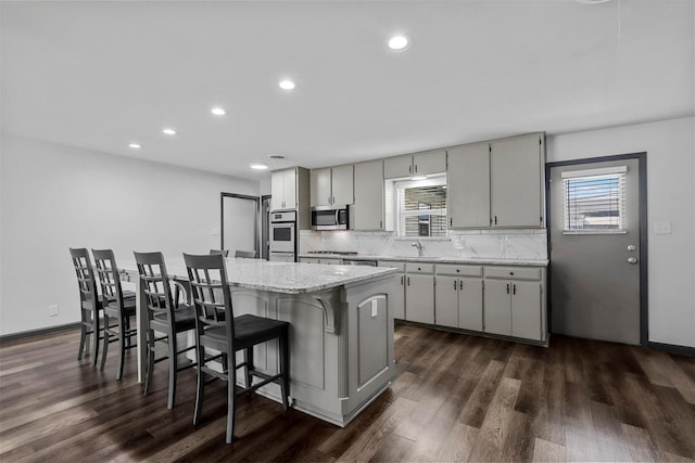 kitchen featuring appliances with stainless steel finishes, a sink, dark wood-style flooring, tasteful backsplash, and a breakfast bar area