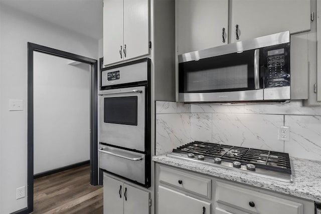 kitchen featuring appliances with stainless steel finishes, a warming drawer, backsplash, white cabinets, and dark wood-style flooring