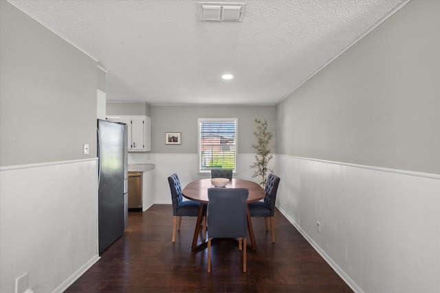 dining area featuring a textured ceiling, visible vents, dark wood-style flooring, and wainscoting