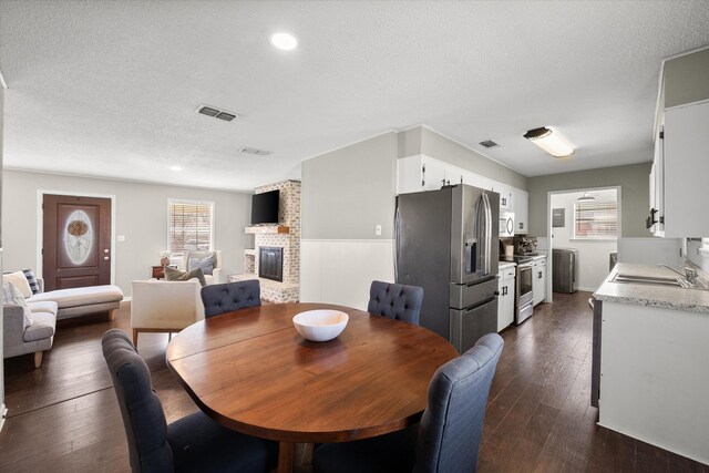 dining room featuring a brick fireplace, visible vents, dark wood-style flooring, and a textured ceiling