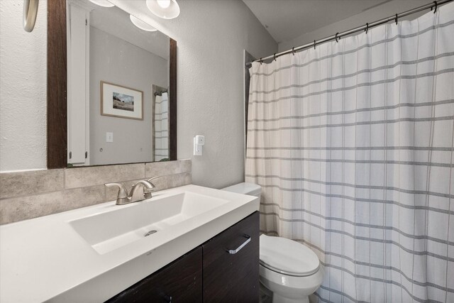 full bathroom featuring curtained shower, toilet, vanity, and a textured wall