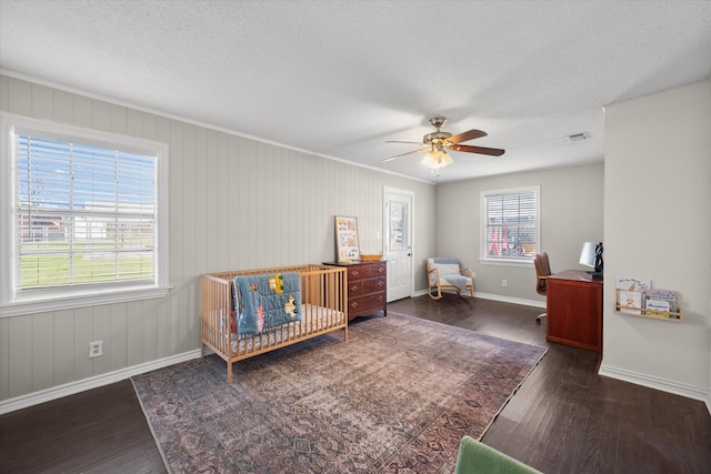 bedroom featuring a crib, a ceiling fan, a textured ceiling, wood finished floors, and baseboards