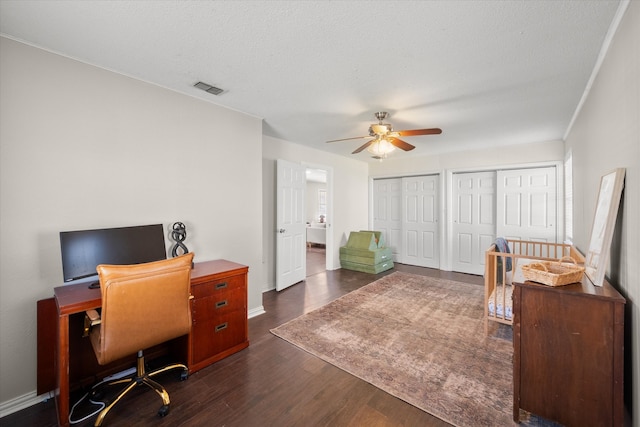 office space featuring a ceiling fan, baseboards, visible vents, dark wood finished floors, and a textured ceiling