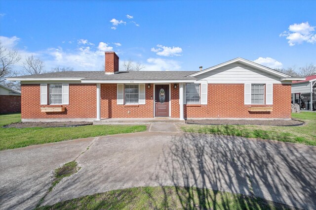 ranch-style house with a front lawn, brick siding, roof with shingles, and a chimney