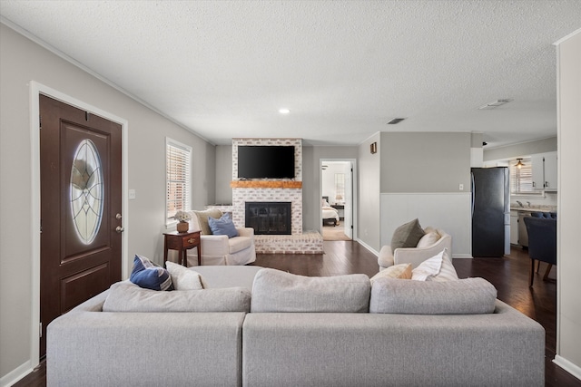 living room featuring visible vents, a textured ceiling, a fireplace, and dark wood-style flooring