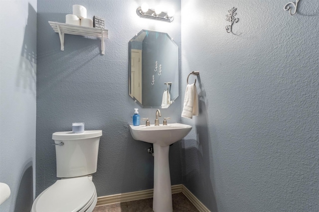 half bathroom with toilet, a textured wall, and baseboards