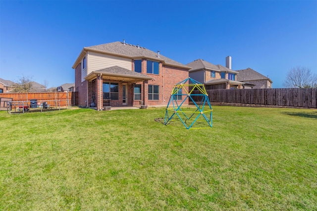 rear view of property featuring brick siding, a fenced backyard, a lawn, and a playground