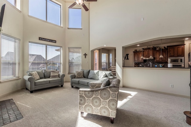 living room featuring arched walkways, light carpet, baseboards, and a ceiling fan