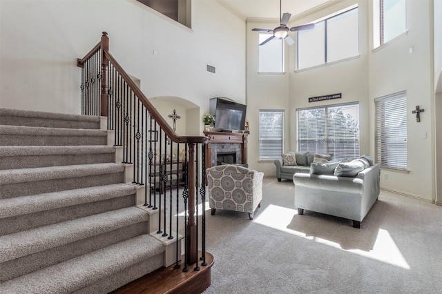 carpeted living room featuring visible vents, baseboards, ceiling fan, stairs, and a tile fireplace