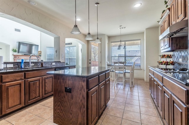 kitchen with light tile patterned floors, visible vents, decorative backsplash, under cabinet range hood, and a center island