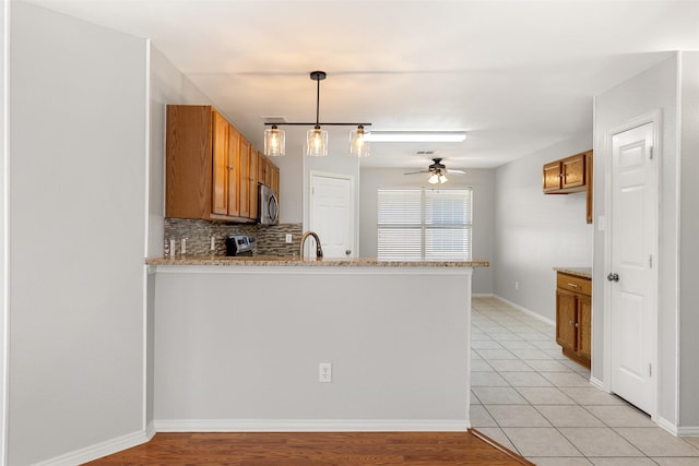 kitchen with stainless steel microwave, brown cabinetry, tasteful backsplash, and a peninsula