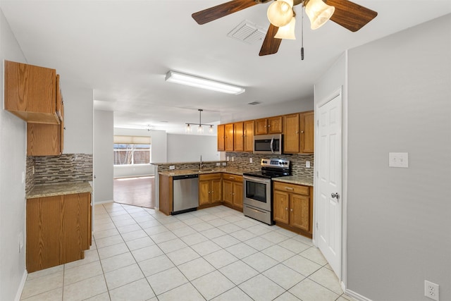 kitchen featuring brown cabinetry, tasteful backsplash, light tile patterned floors, a peninsula, and stainless steel appliances