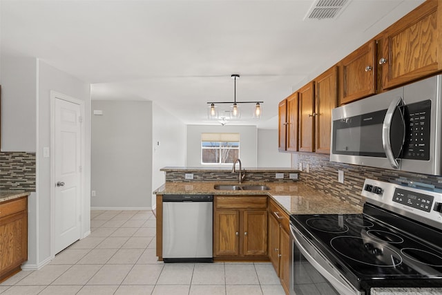 kitchen with brown cabinetry, backsplash, a sink, a peninsula, and stainless steel appliances
