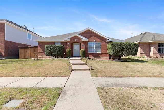 ranch-style house featuring brick siding, fence, a shingled roof, and a front lawn