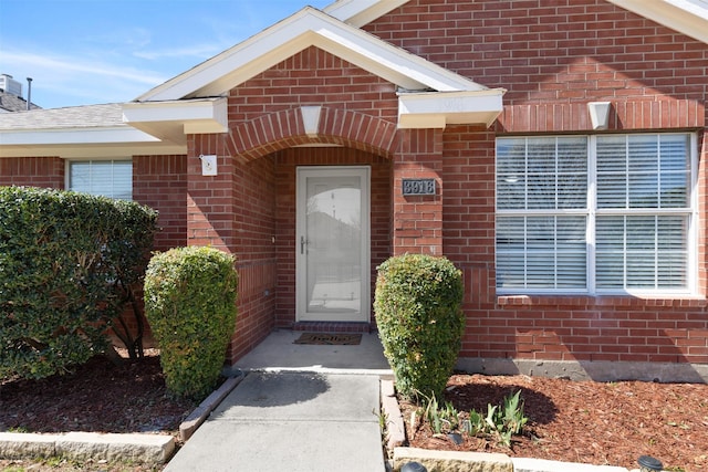 property entrance featuring brick siding and roof with shingles