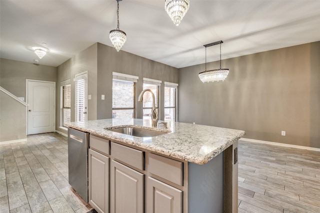 kitchen featuring a sink, wood finish floors, an island with sink, light stone counters, and stainless steel dishwasher