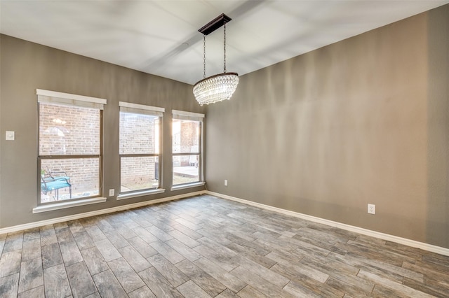 spare room featuring an inviting chandelier, wood finished floors, and baseboards