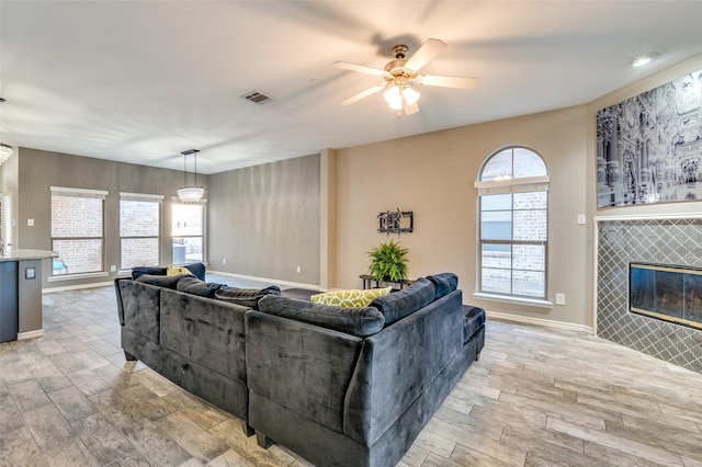 living area featuring visible vents, light wood finished floors, baseboards, ceiling fan, and a tile fireplace