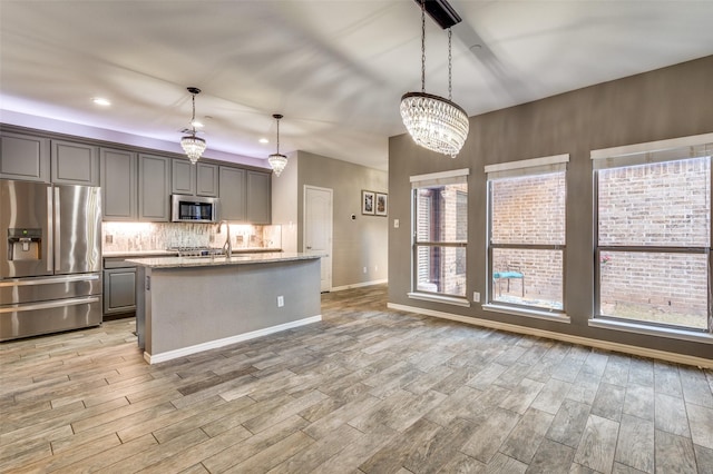 kitchen with gray cabinetry, a center island with sink, tasteful backsplash, stainless steel appliances, and light wood finished floors