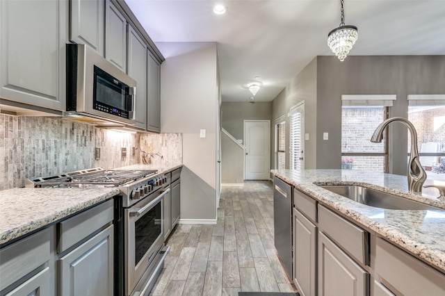 kitchen featuring light wood-style flooring, gray cabinets, a sink, stainless steel appliances, and decorative backsplash