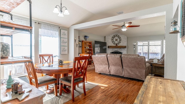 dining area featuring visible vents, ceiling fan with notable chandelier, wood finished floors, a fireplace, and vaulted ceiling