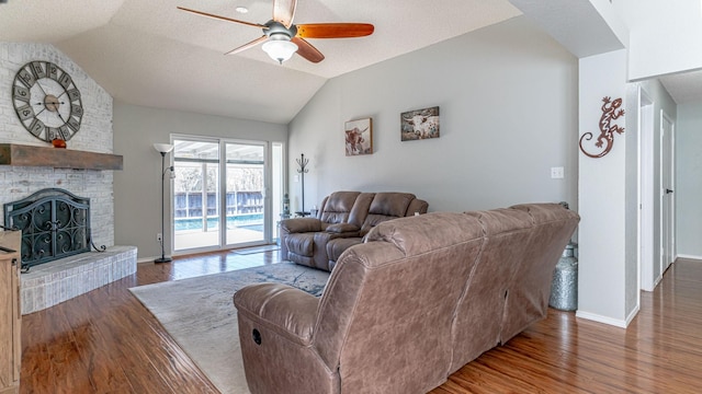 living area featuring a ceiling fan, wood finished floors, a fireplace, and lofted ceiling