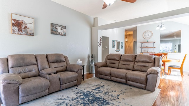 living room with light wood finished floors, ceiling fan with notable chandelier, and lofted ceiling