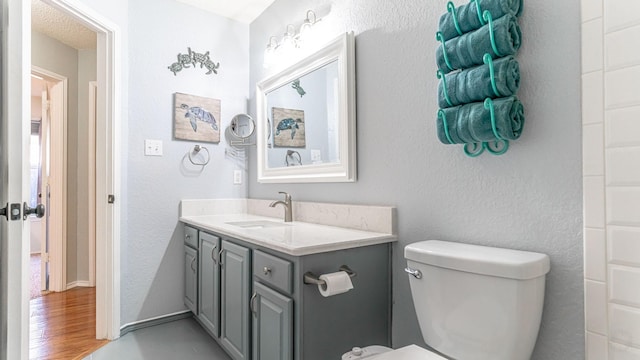 bathroom with vanity, toilet, a textured wall, and baseboards