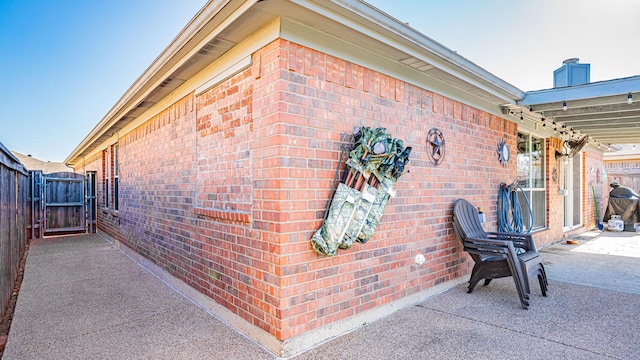 view of side of home featuring brick siding, a gate, a patio, and fence