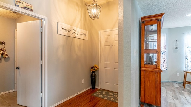 hallway featuring an inviting chandelier, baseboards, light wood-type flooring, and a textured ceiling