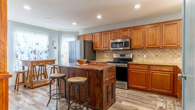 kitchen featuring tasteful backsplash, butcher block counters, light wood-type flooring, brown cabinetry, and stainless steel appliances