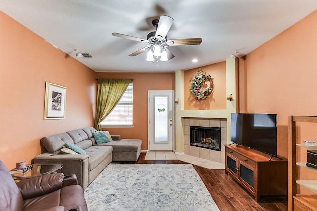 living room featuring dark wood-style floors, baseboards, visible vents, ceiling fan, and a tiled fireplace