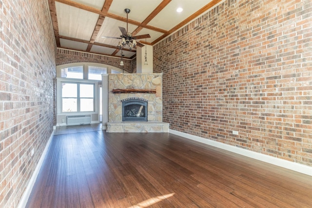 unfurnished living room featuring brick wall, a fireplace, an AC wall unit, wood-type flooring, and a towering ceiling