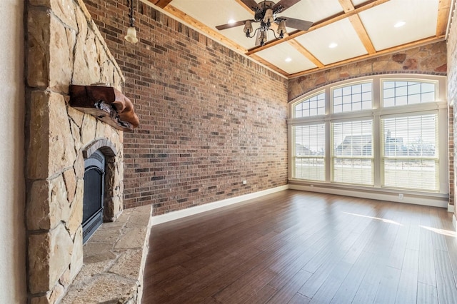 unfurnished living room with wood finished floors, brick wall, beam ceiling, a fireplace, and ceiling fan