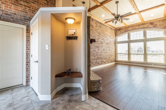 interior space with a ceiling fan, baseboards, coffered ceiling, brick wall, and beamed ceiling