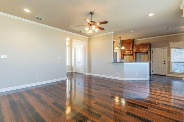 unfurnished living room with visible vents, dark wood-type flooring, ceiling fan with notable chandelier, crown molding, and baseboards