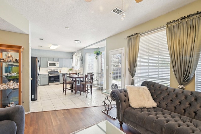 living area featuring visible vents, light wood finished floors, and a textured ceiling