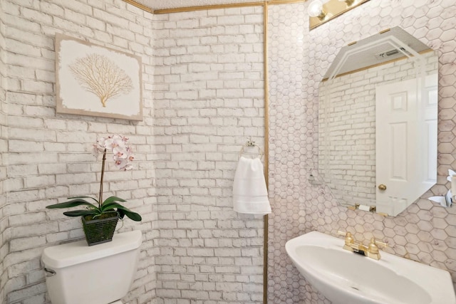 half bath with decorative backsplash, brick wall, toilet, and a sink