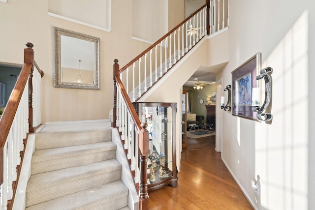 stairs featuring wood finished floors, baseboards, and a towering ceiling