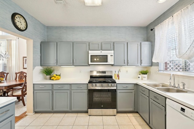 kitchen with gray cabinetry, a sink, a textured ceiling, white appliances, and light countertops