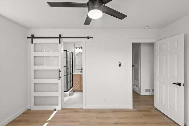 unfurnished bedroom featuring a barn door, baseboards, visible vents, and light wood-type flooring