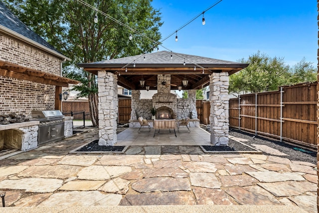 view of patio / terrace with a gazebo, an outdoor stone fireplace, a fenced backyard, area for grilling, and an outdoor kitchen