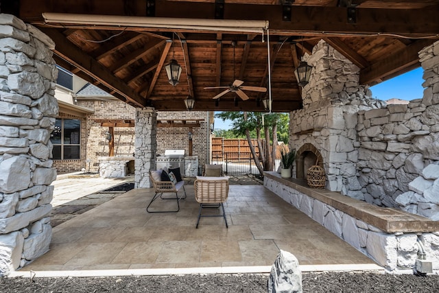 view of patio / terrace with a ceiling fan, fence, an outdoor stone fireplace, a gazebo, and a grill