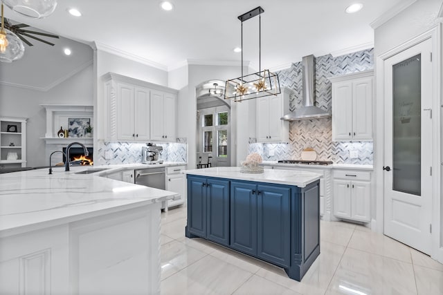 kitchen featuring a kitchen island, a sink, blue cabinets, white cabinetry, and wall chimney exhaust hood