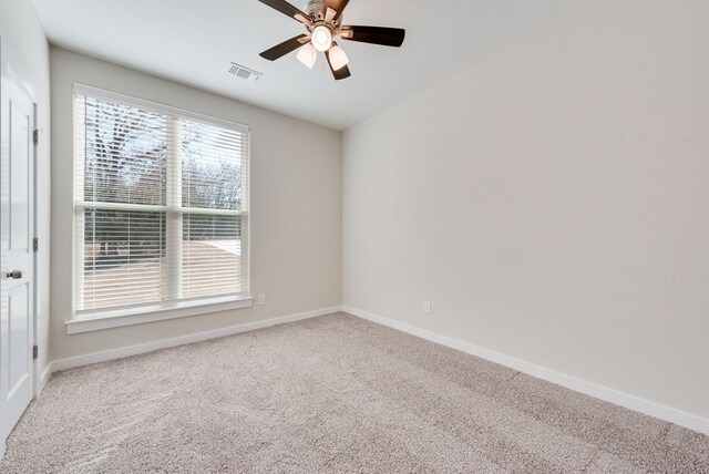 carpeted spare room with visible vents, baseboards, and ceiling fan