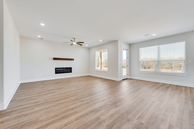 unfurnished living room with light wood-type flooring, visible vents, a healthy amount of sunlight, and a glass covered fireplace